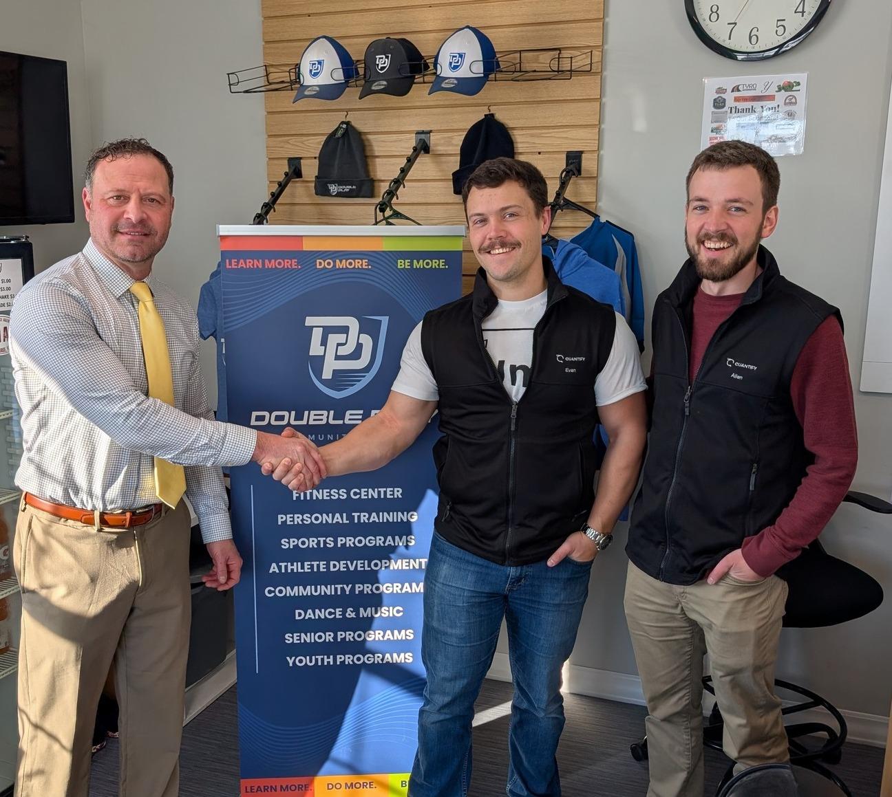 Double Play Community Center's executive director shaking hands with the Quantify team in front of a Double Play program banner