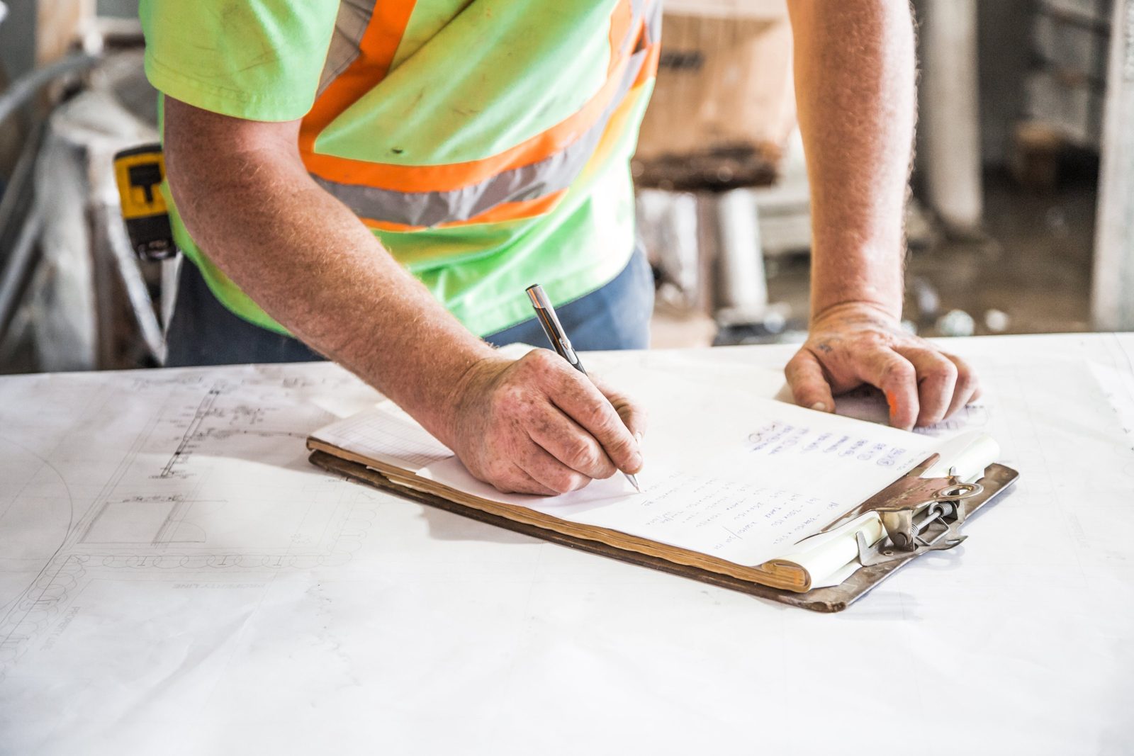 A building codes inspector in a high-visibility vest filling out an inspection form on a clipboard over a set of property plans